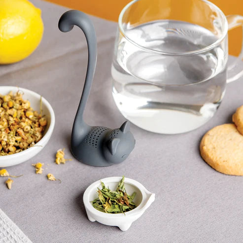 Tea infuser shaped like a cat with tea leaves and a glass of water on a table.